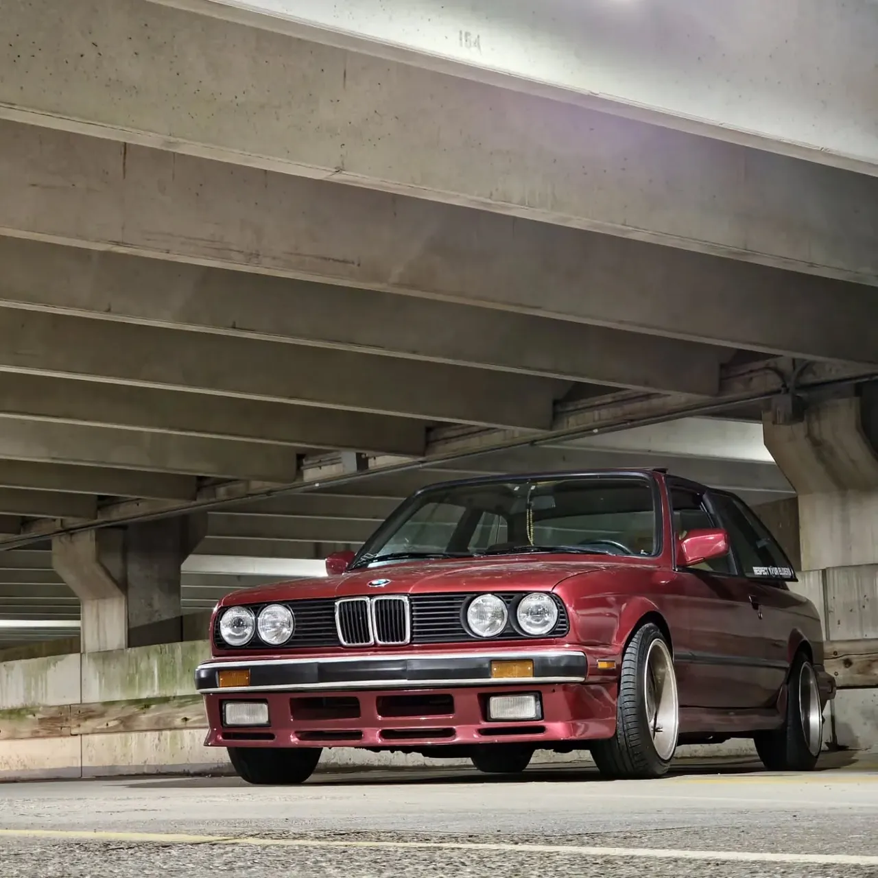 The burgundy E30 head-on, showing its quad round headlights