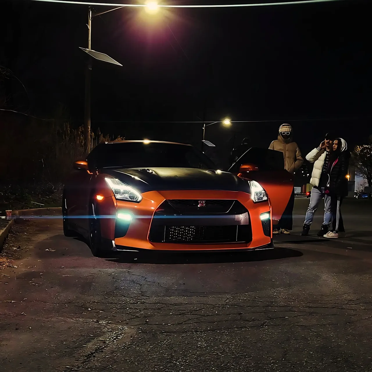 An orange Nissan GT-R at a night meet, with people standing around it