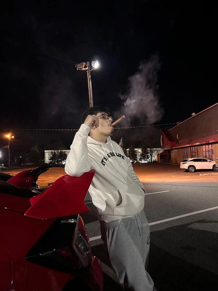 A club member leaning on a red car's rear wing at a night meet