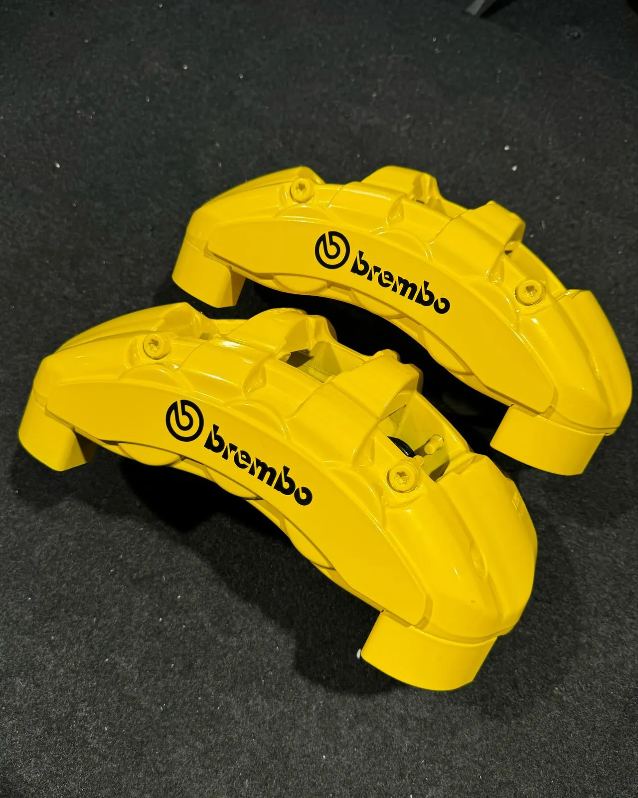 Two yellow powder-coated Brembo calipers on a dark mat